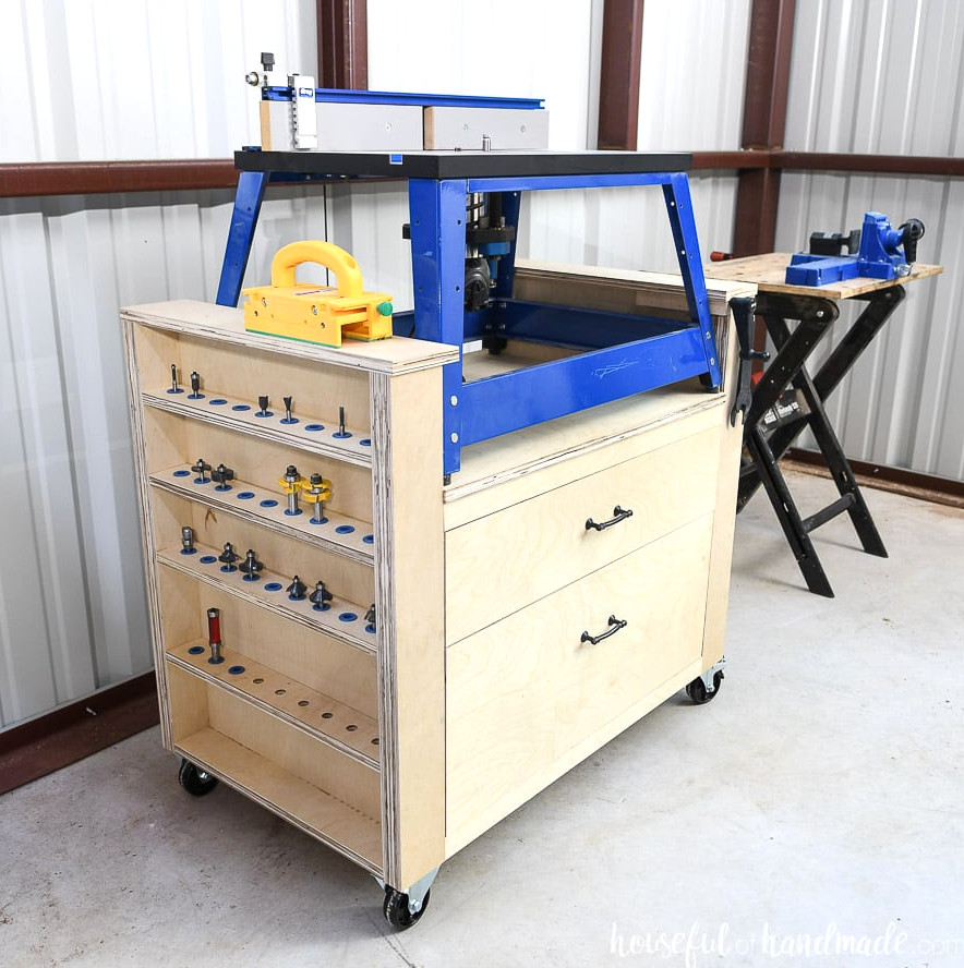 Angled shot of the DIY bench top router table made from plywood with a blue framed bench top router on it showing the side with the router bits storage.