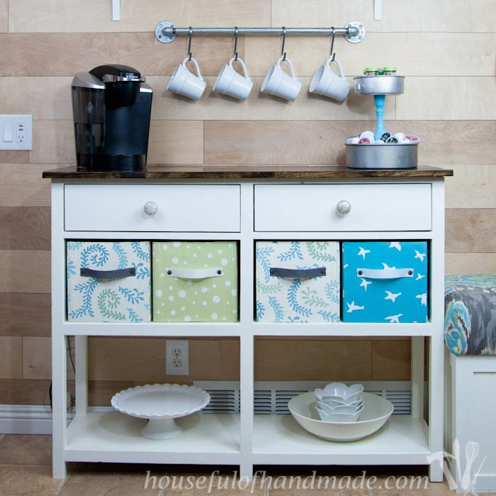 White painted coffee bar table with dark stained wood top and drawers for storage.