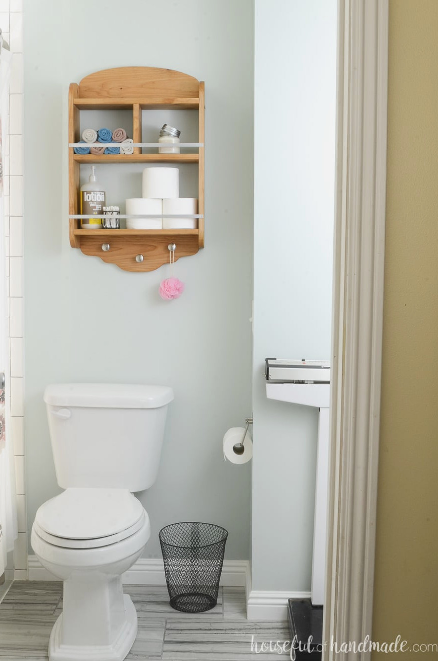 View of the bathroom featuring the new storage shelves above the toilet. Knotty alder shelves hold various bathroom essentials.