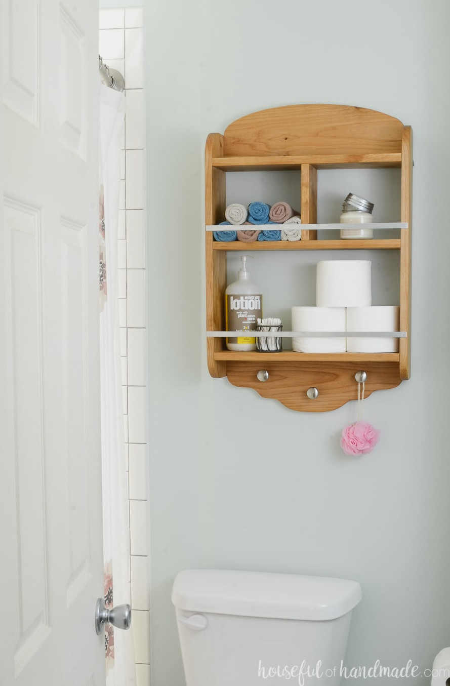 DIY bathroom storage shelves mounted above the toilet for additional organization. Wooden shelves display toilet paper, lotion and washcloths.
