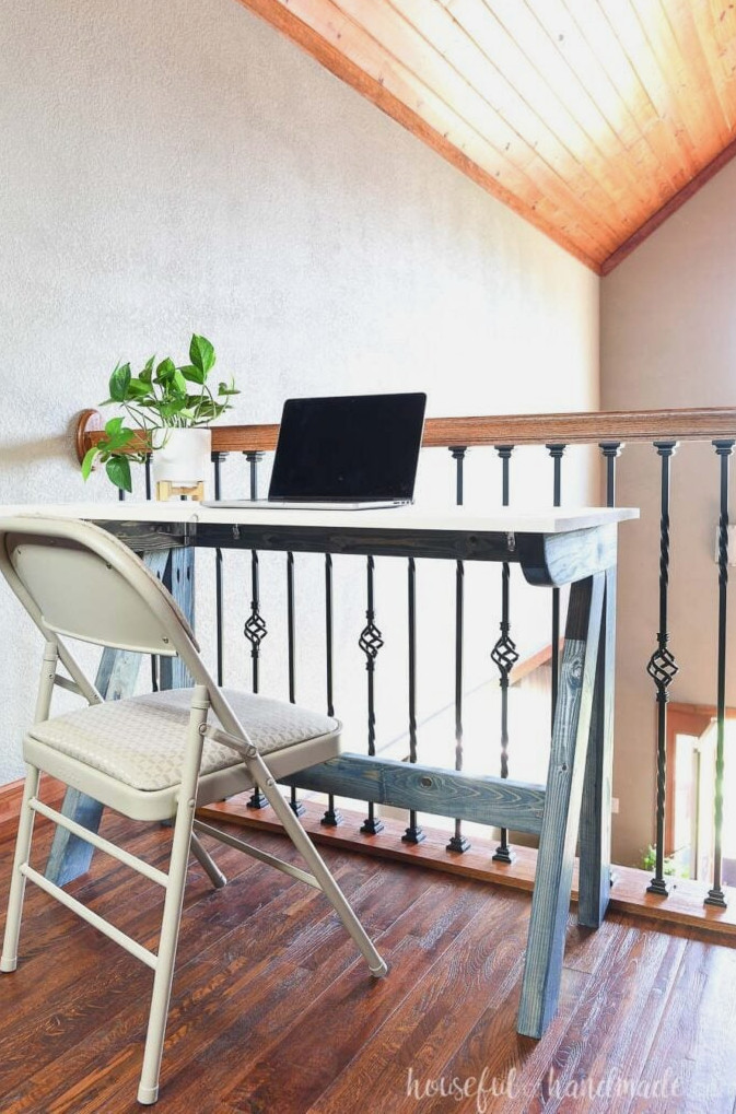 Blue and white desk constructed from 2x4s placed in the loft with a laptop resting on top.