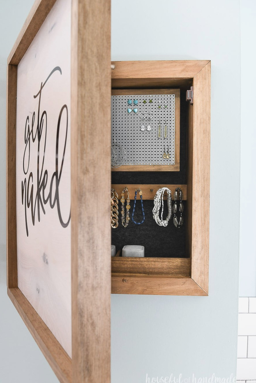 Wood sign with get naked script on it opening to reveal wall jewelry organizer.