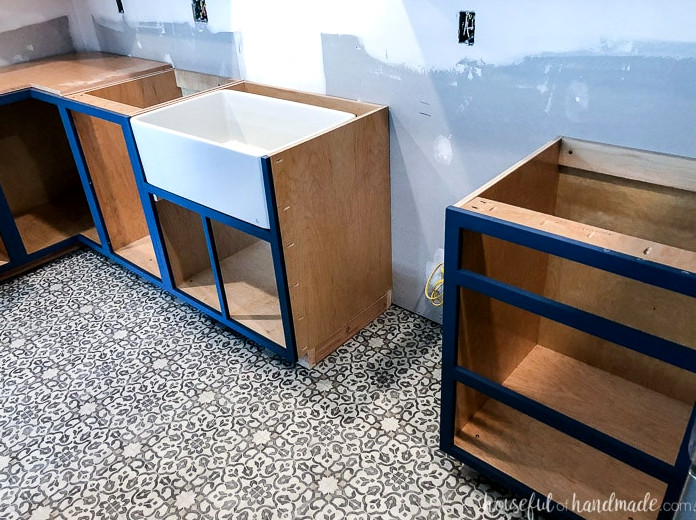 Navy blue face-frame base cabinets installed in a kitchen before the doors were added, including a custom apron front sink base cabinet.