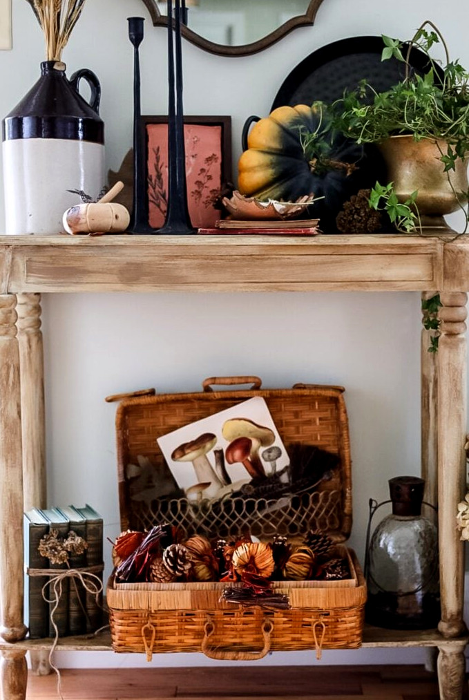 Entryway table decorated for Fall with plants, pumpkins, books, candleticks and more