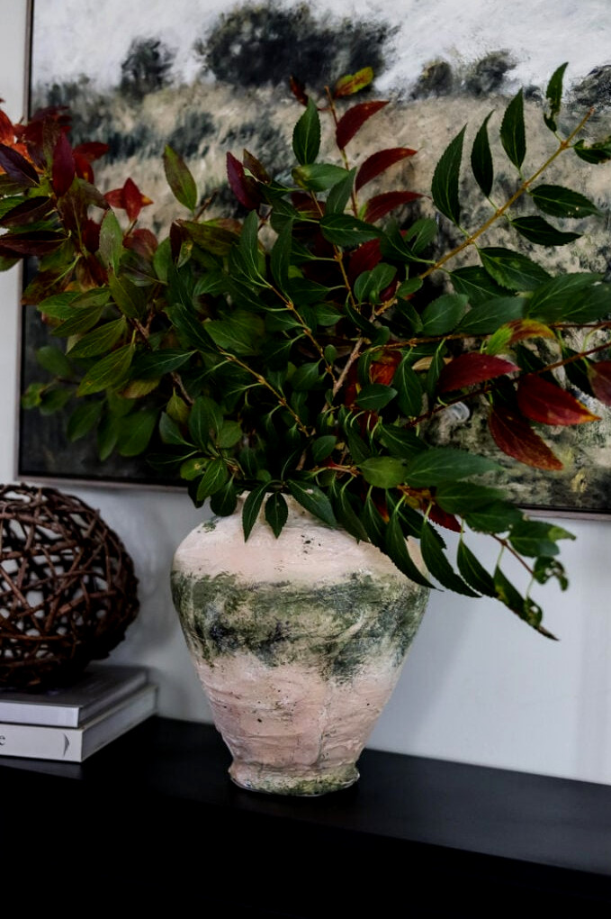 rustic looking vase filled with green branches on a mantle.