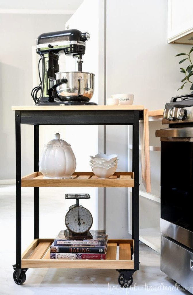 Black-and-wood modern rolling kitchen cart with a stand mixer on top beside a stove.