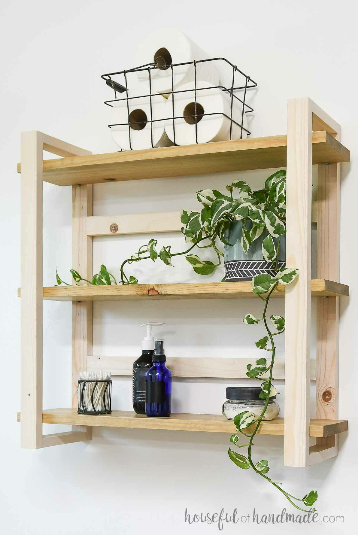 DIY bathroom wall shelves holding a plant, rolls of toilet tissue, and bottles of creams.