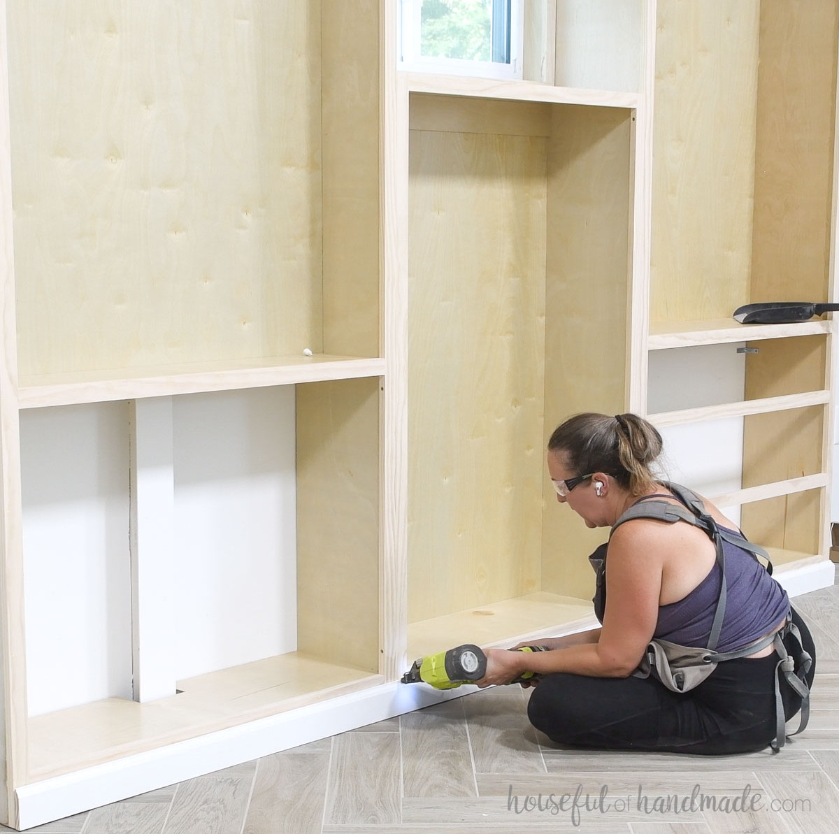 Installing baseboards along the front of the built-in bookcases.