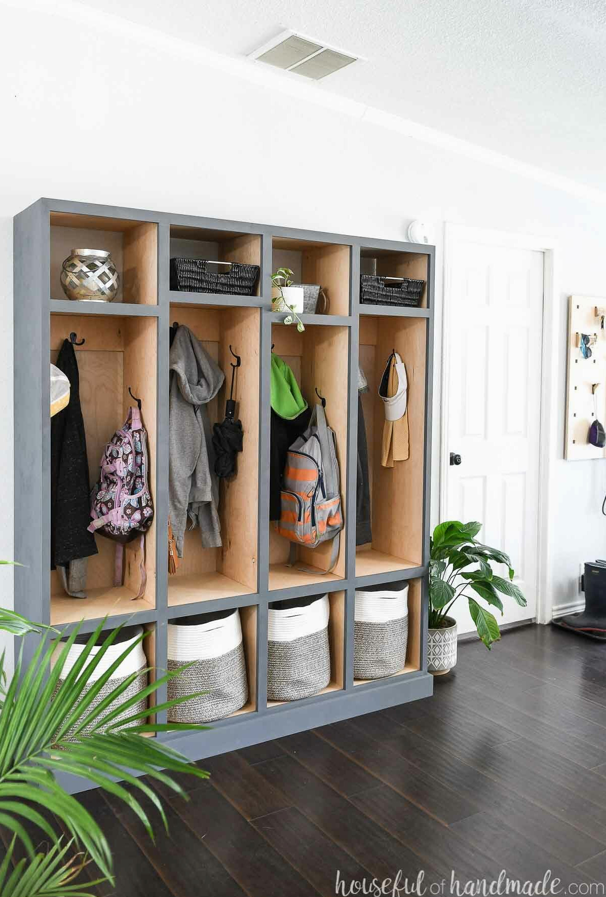 DIY mudroom storage lockers featuring a natural wood interior and gray-blue painted exterior in an entryway filled with coats and backpacks. 