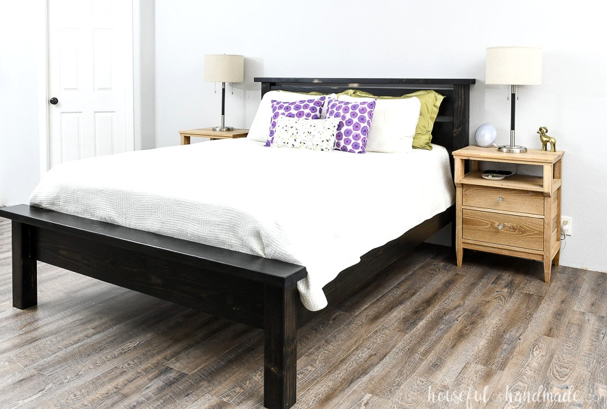 Simple DIY bed frame, stained black, with a white comforter and bright pillows. 