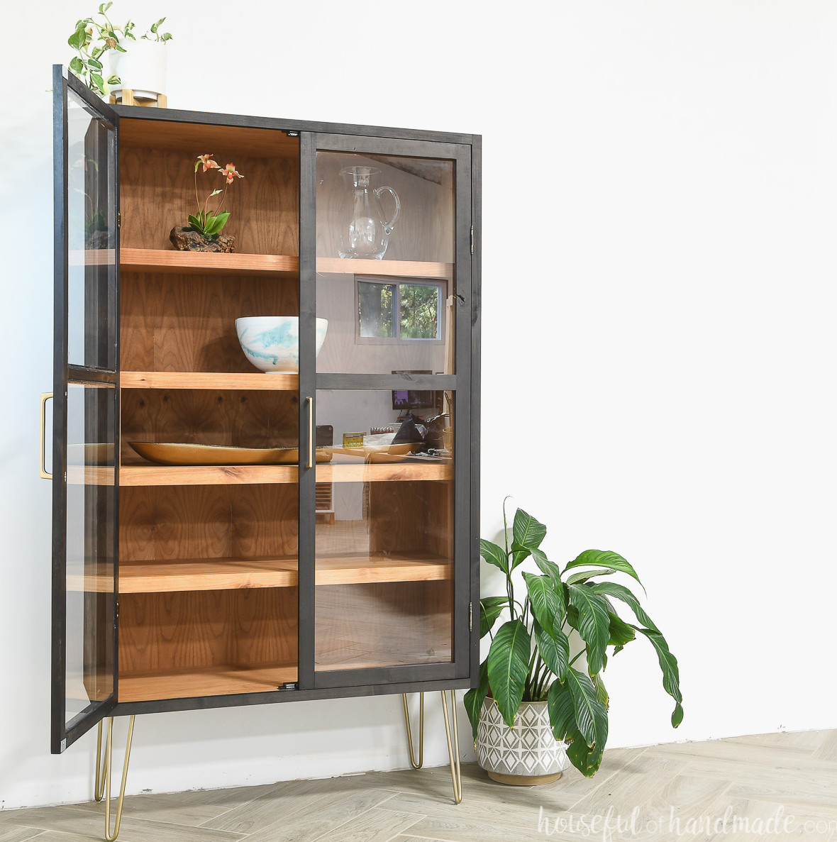 Stunning black DIY display cabinet featuring gold accents and a stained wood interior, with one door open to reveal the shelves inside. 