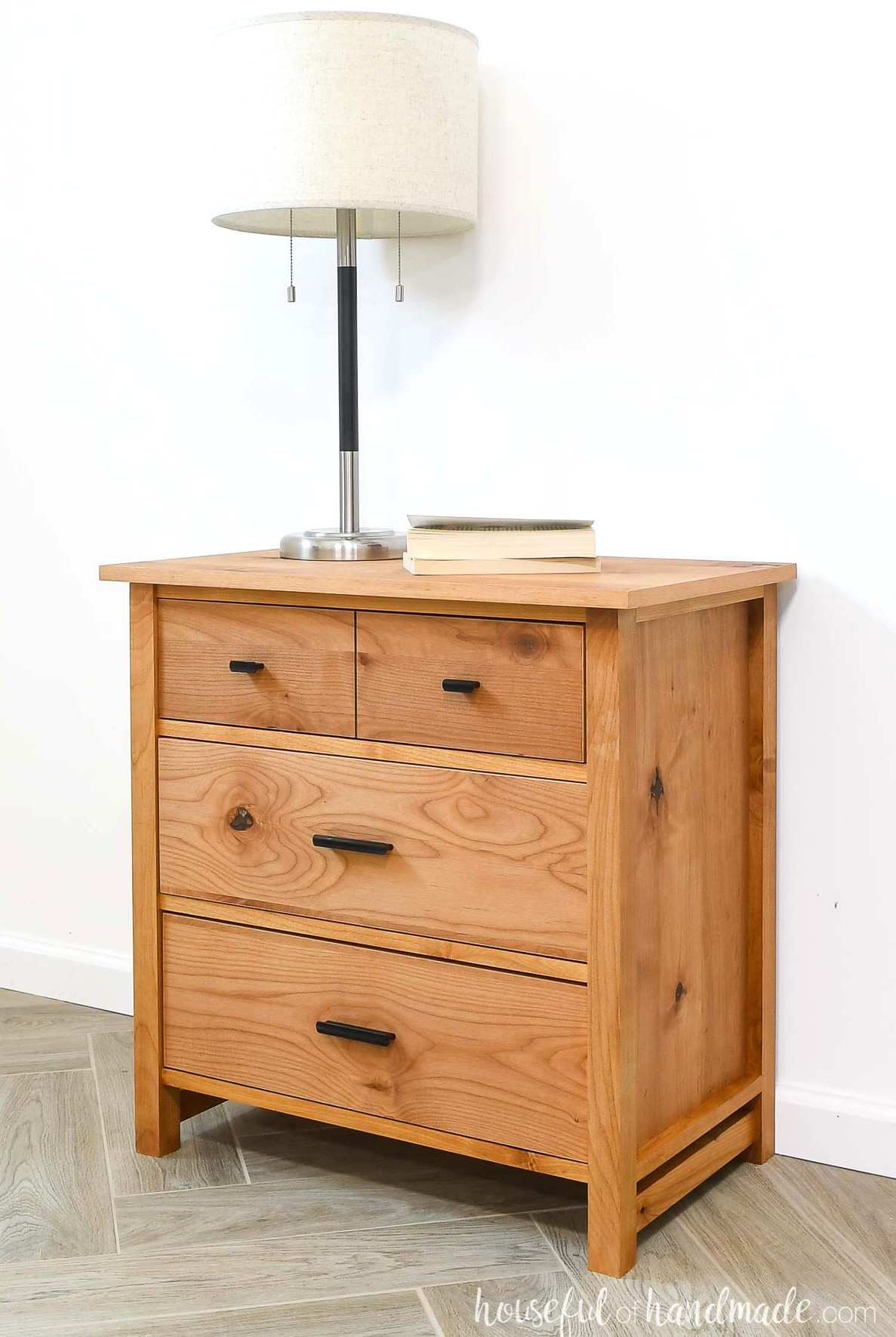 Simple three-drawer nightstand with a top drawer styled to resemble two small drawers, crafted from warm-toned wood. 