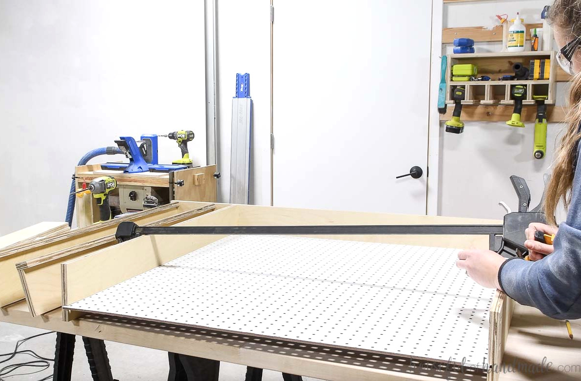 Sliding the pegboard into the cabinet frame and using a clamp to hold it in place.