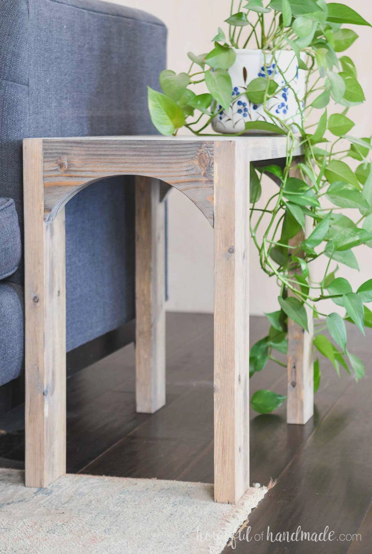 Narrow side table featuring an arch on the front beside a blue sofa.