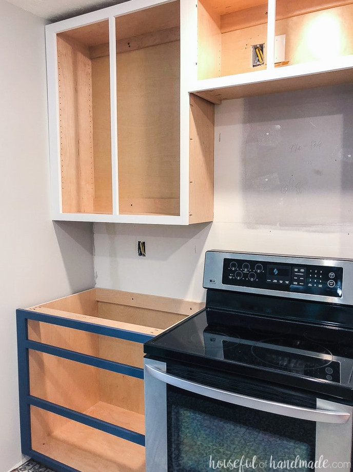 Kitchen with cabinets installed without cabinet doors yet. Base cabinet is a drawer base and uppers are over stove.