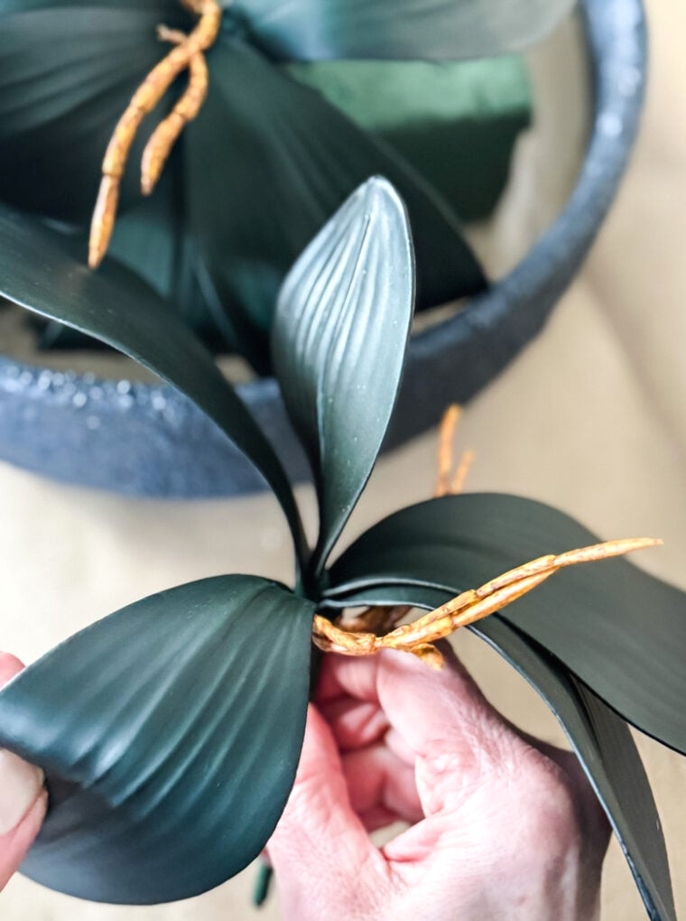 a hand holding a fake orchid leaf bunch