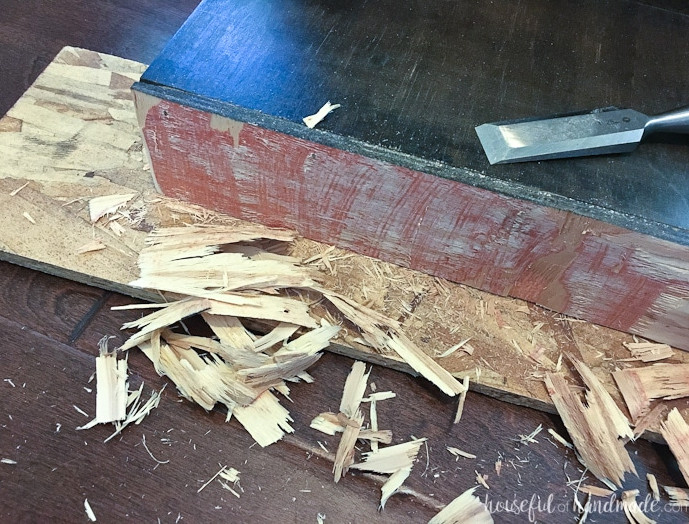 Toe kick being shaved smaller with a chisel and lots of chips of wood on the floor next to it.