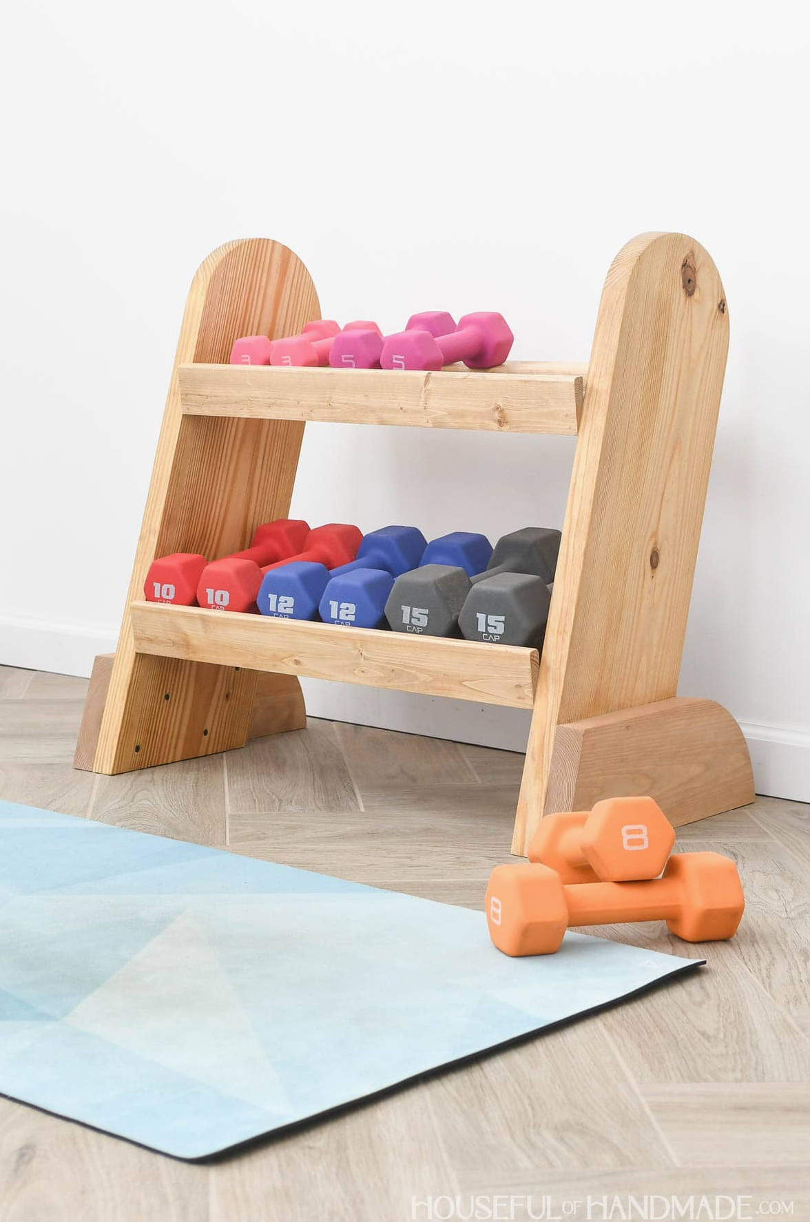 Wooden weight rack holding dumbbells and positioned beside additional weights on the floor.