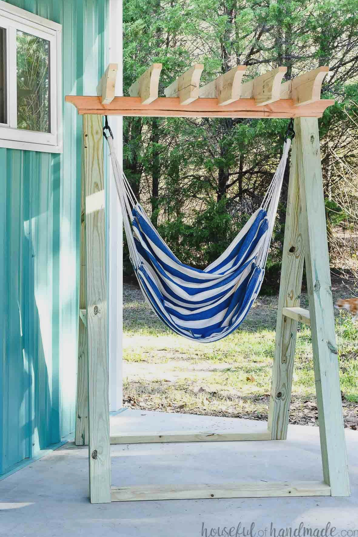 Blue and white striped fabric hammock chair hanging from a wooden chair stand on a porch.