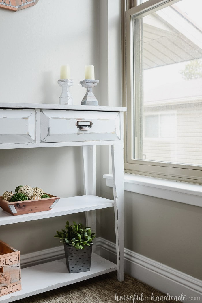 White farmhouse console table positioned beside the window. This compact table includes drawers and two shelves. Housefulofhandmade.com