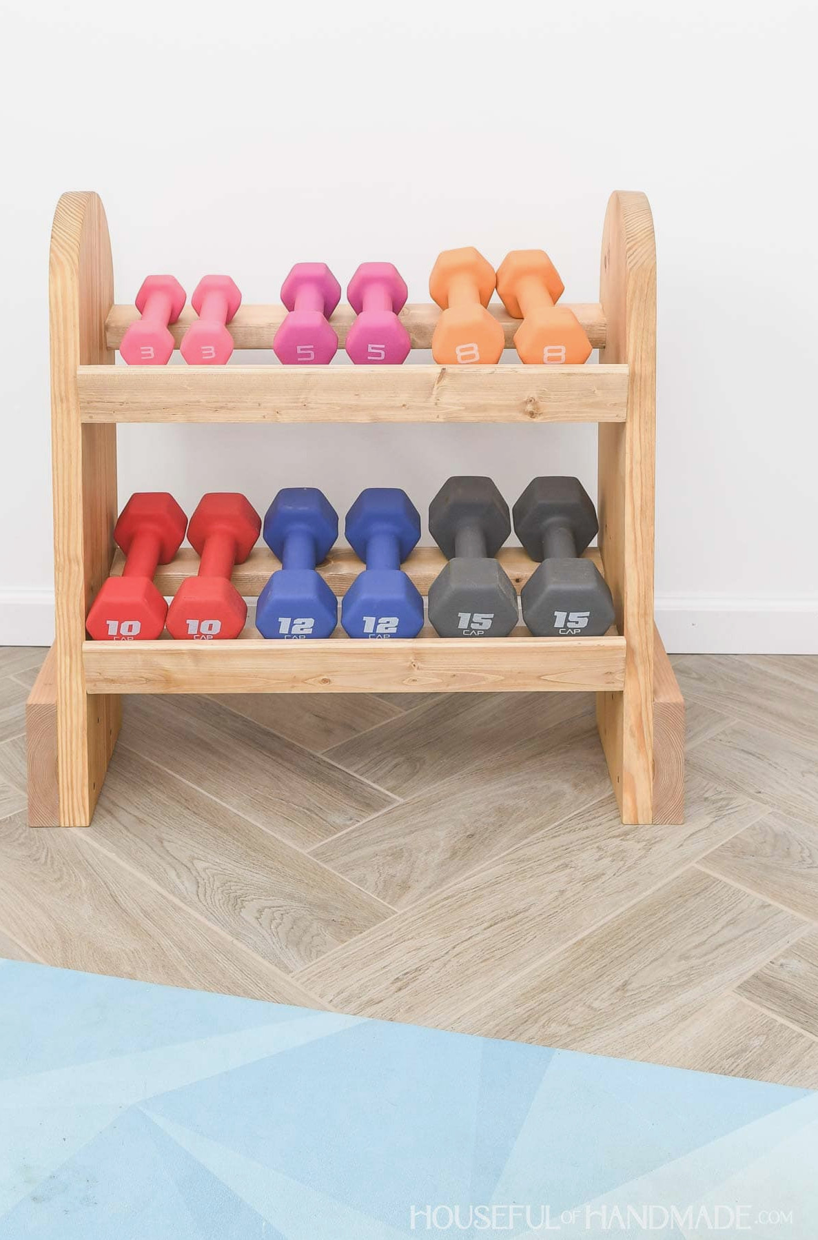 Six weights resting on a homemade wooden dumbbell rack.
