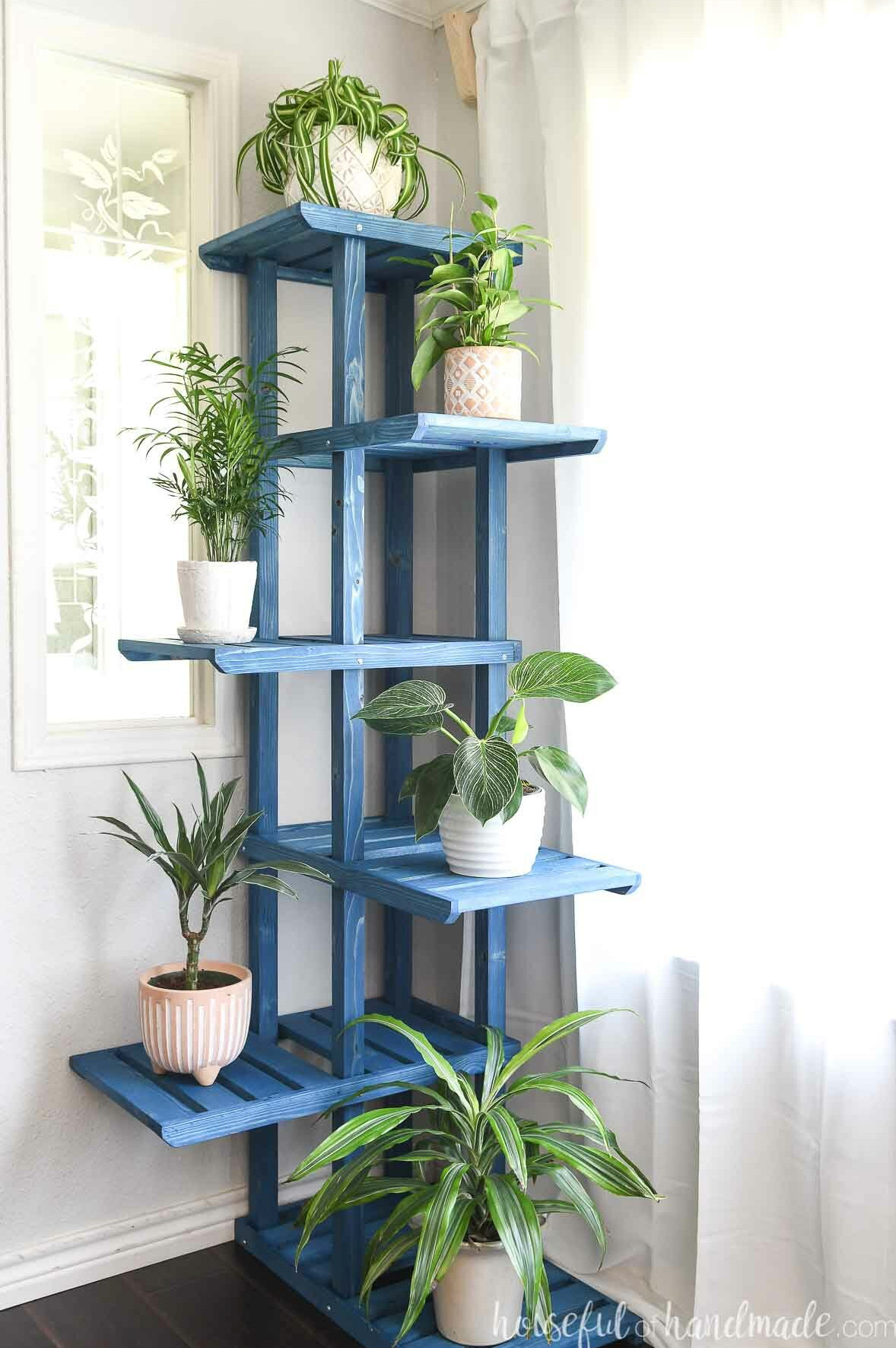 Tiered corner plant stand placed beside a window and filled with houseplants.