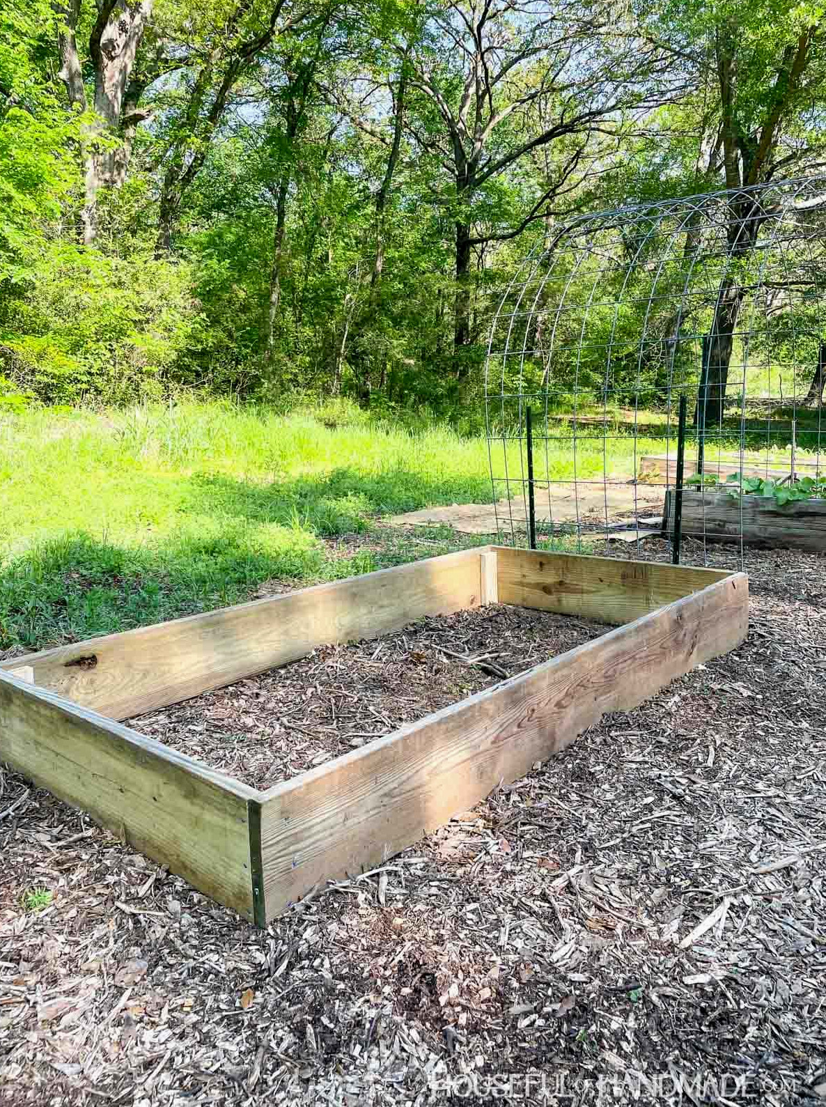 Empty DIY raised garden bed constructed from 2x boards with mulch surrounding it.