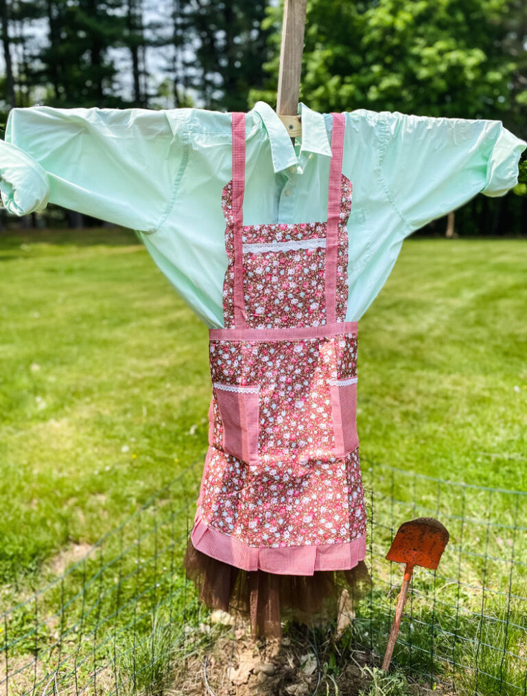 scarecrow in garden with green shirt and flowered apron