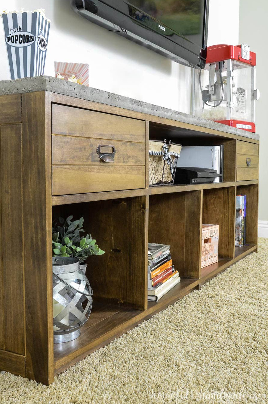 Angled view of a medium-brown stained TV stand featuring 2 drawers and a concrete surface.