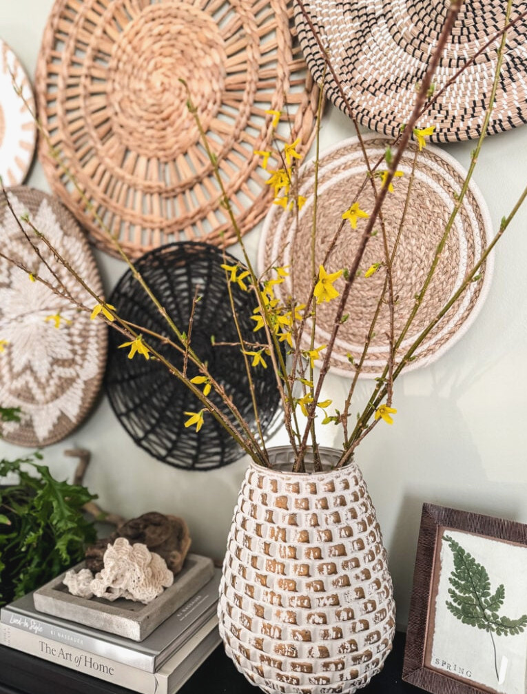 forsythia in vase with basket wall behind it
