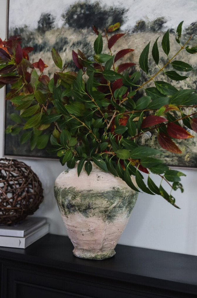 rustic looking vase filled with green branches on a mantle.