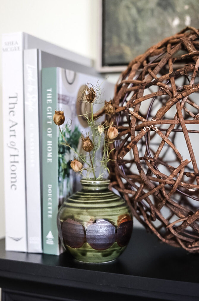 a small green pottery vase filled with dried flower pods, a stack of home decor books is in the background.