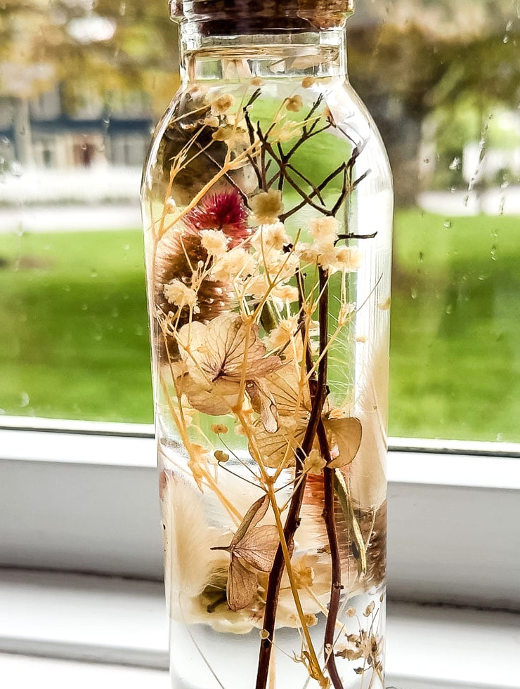 a herbarium bottle in a white windowsill with green grass outside of it.