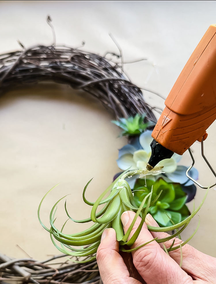 hot glue gun gluing a fake succulent to a wreath